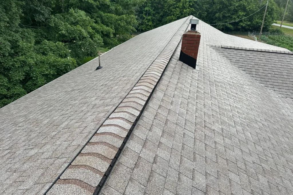 Newly installed shingle roof with a clean ridge vent and chimney flashing, showing even shingle alignment across the long roof slope.