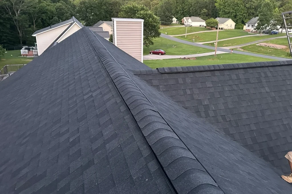 A new dark shingle roof with ridge venting on a residential home, overlooking a suburban neighborhood and tree line.
